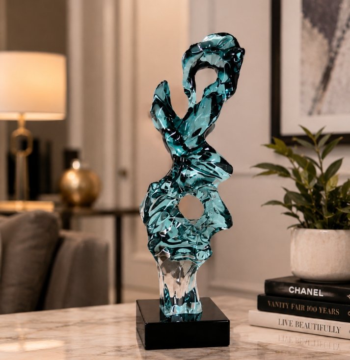 Luxury aqua crystal glass sculpture with flowing abstract organic forms mounted on a black pedestal, displayed as a contemporary decorative centerpiece in an elegant modern interior.