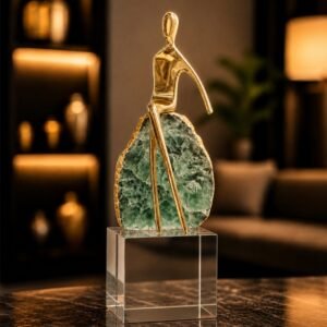 Luxury abstract sculpture featuring a gold-toned figure, green crystal-inspired centerpiece, and transparent pedestal base, displayed as a sophisticated decorative accent in a modern interior.