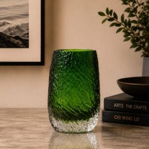 Luxury emerald-green textured glass vase with a clear crystal base, displayed as an elegant decorative accent on a marble surface in a sophisticated contemporary interior.