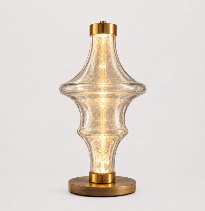 Luxury sculptural glass table lamp with a transparent art glass body, warm glowing illumination, and brushed gold accents, designed for elegant contemporary interiors.