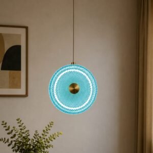 Luxury blue art glass pendant light with a circular geometric textured design, brushed gold center accent, and elegant ambient illumination in a sophisticated contemporary interior.