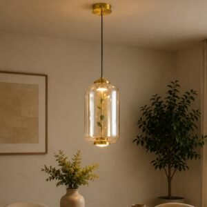 Luxury glass pendant light with a clear cylindrical shade, botanical decorative element, gold accents, and warm ambient illumination, suspended in a sophisticated contemporary interior.